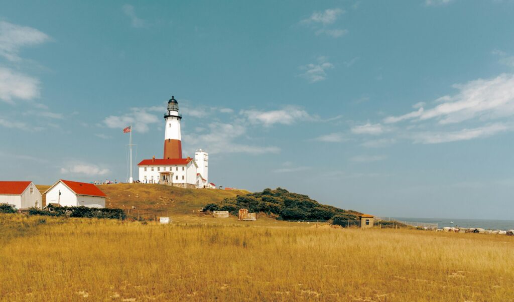 Scenic view of Montauk Point Lighthouse on a sunny day, featuring a vast grassy field and clear blue skies.